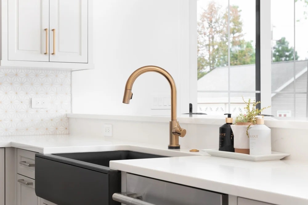 Golden sink on white countertop and white cabinetry with windows