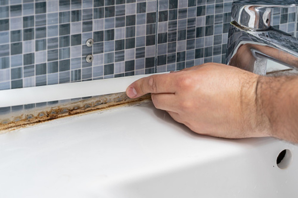 Mold and rust growing in tile joints in a damp poorly ventilated bathroom with high humidity. hands close up