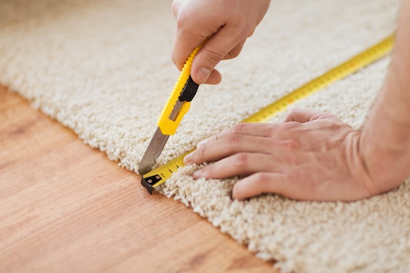 repair, building and home concept - close up of male hands cutting carpet with blade