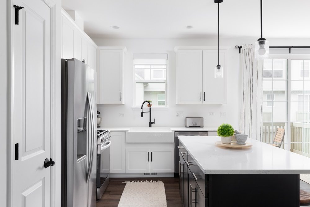 A modern kitchen with white cabinets and black hardware detailing.