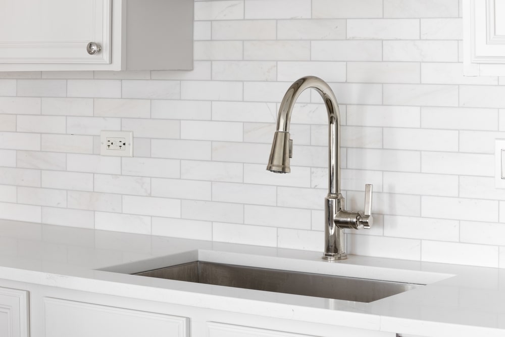 Plumber installing a modern kitchen sink faucet in a newly remodeled kitchen