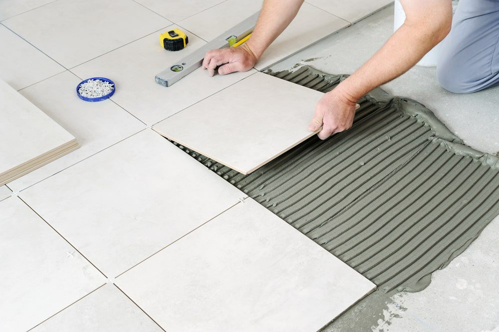 Installer setting ceramic floor tile with leveling clips and metal edge profile for a clean finish