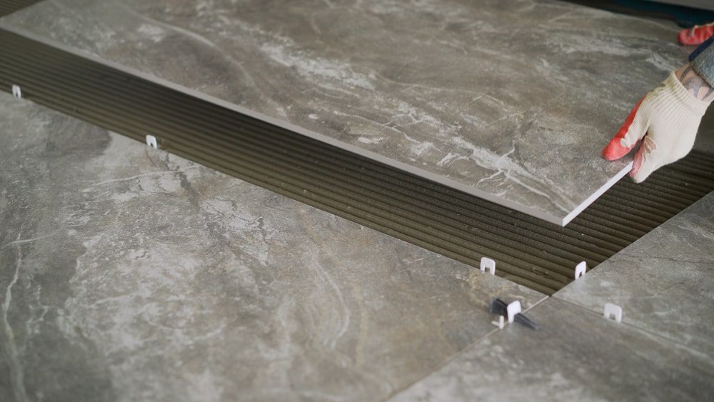Installer setting ceramic floor tile with leveling clips and metal edge profile for a clean finish