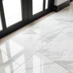 Installer setting ceramic floor tile with leveling clips and metal edge profile for a clean finish