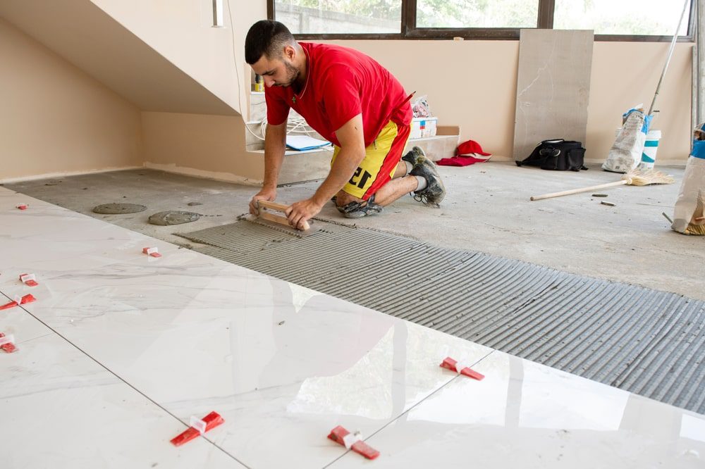 Installer setting ceramic floor tile with leveling clips and metal edge profile for a clean finish
