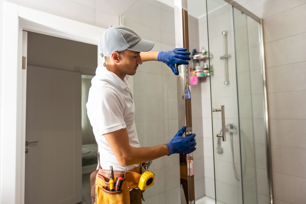 Installer aligning a frameless glass shower door with a level and suction cups over tiled walls