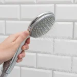 Hands wrapping PTFE tape on a shower arm before installing a new shower head in an apartment bathroom