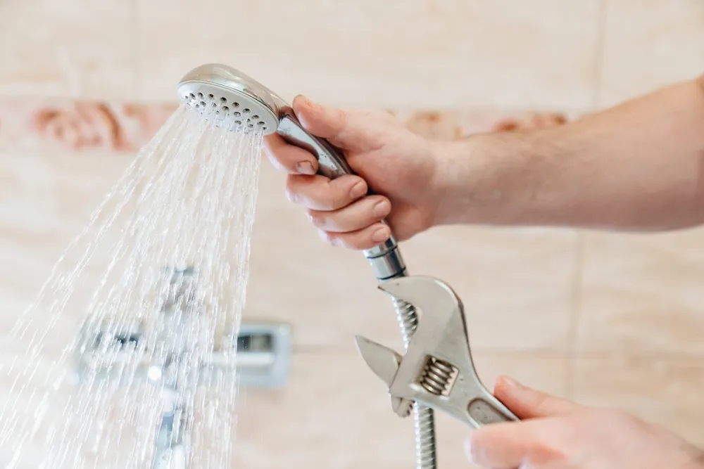 Hands wrapping PTFE tape on a shower arm before installing a new shower head in an apartment bathroom
