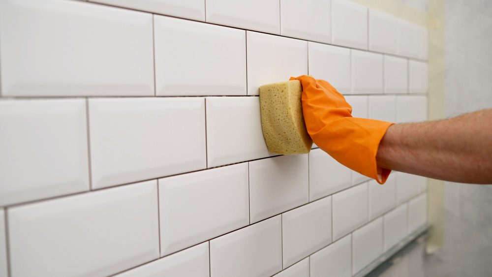  Close-up of shower wall as fresh grout is applied and tooled between ceramic tiles
