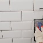 Close-up of shower wall as fresh grout is applied and tooled between ceramic tiles