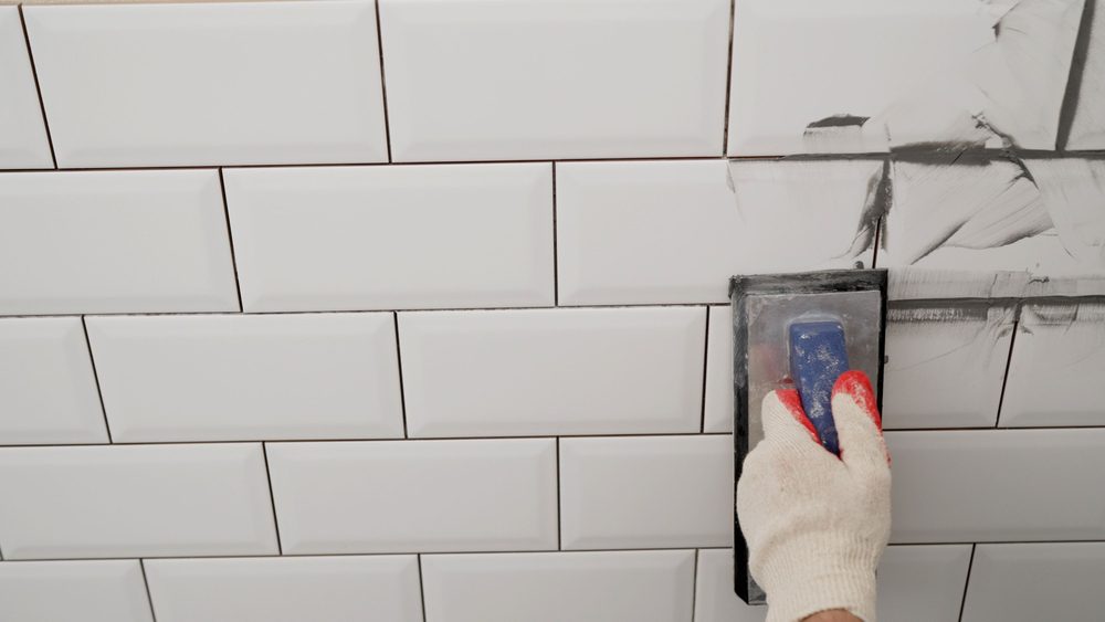 Close-up of shower wall as fresh grout is applied and tooled between ceramic tiles