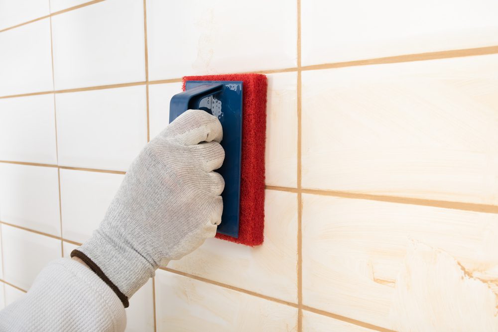  Close-up of shower wall as fresh grout is applied and tooled between ceramic tiles
