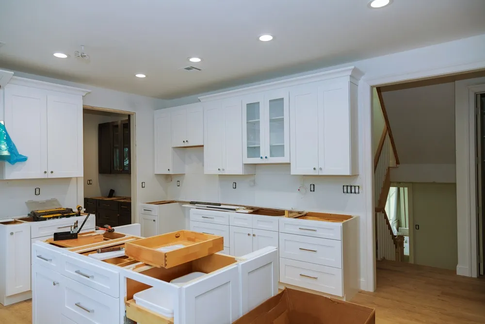 Carpenter fitting white crown molding above kitchen cabinets with a miter saw and finish nailer.