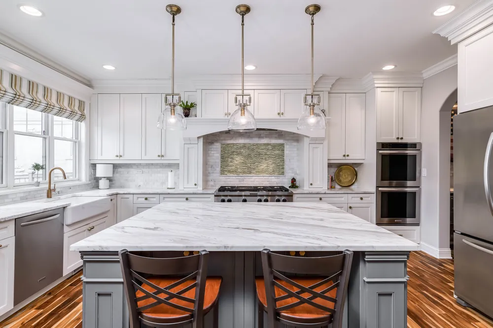 Carpenter fitting white crown molding above kitchen cabinets with a miter saw and finish nailer.