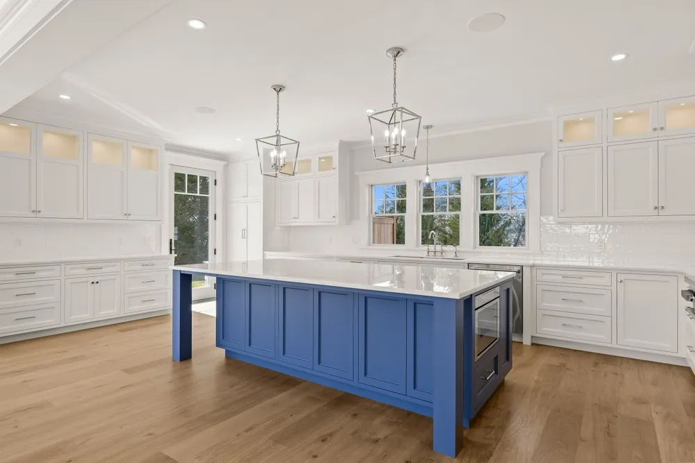 Carpenter fitting white crown molding above kitchen cabinets with a miter saw and finish nailer.