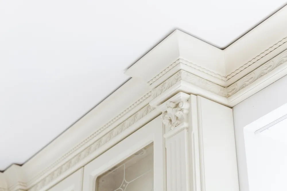 Carpenter fitting white crown molding above kitchen cabinets with a miter saw and finish nailer.
