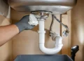 Homeowner replacing a stainless-steel basket strainer in a kitchen sink with the drain parts arranged in order.