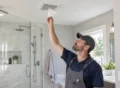 Remodeling professional holding a tissue near a newly installed ceiling exhaust fan to test airflow.