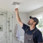 Remodeling professional holding a tissue near a newly installed ceiling exhaust fan to test airflow.