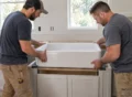 Carpenter securing wooden ledgers and a plywood support platform inside a farmhouse sink cabinet.